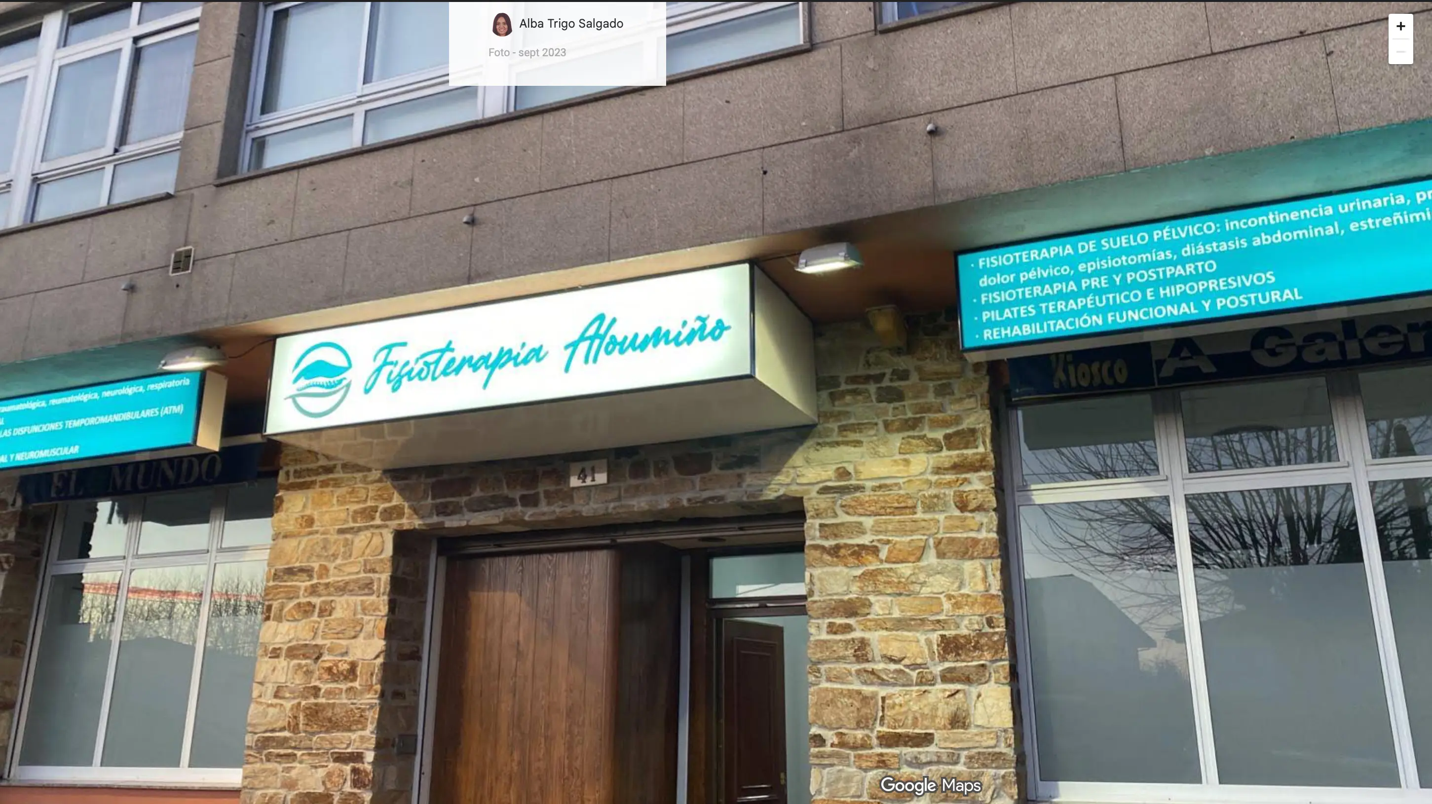 Fachada de Fisioterapia Aloumiño: el rótulo de la clínica sobre la entrada de piedra y paneles con los tratamientos